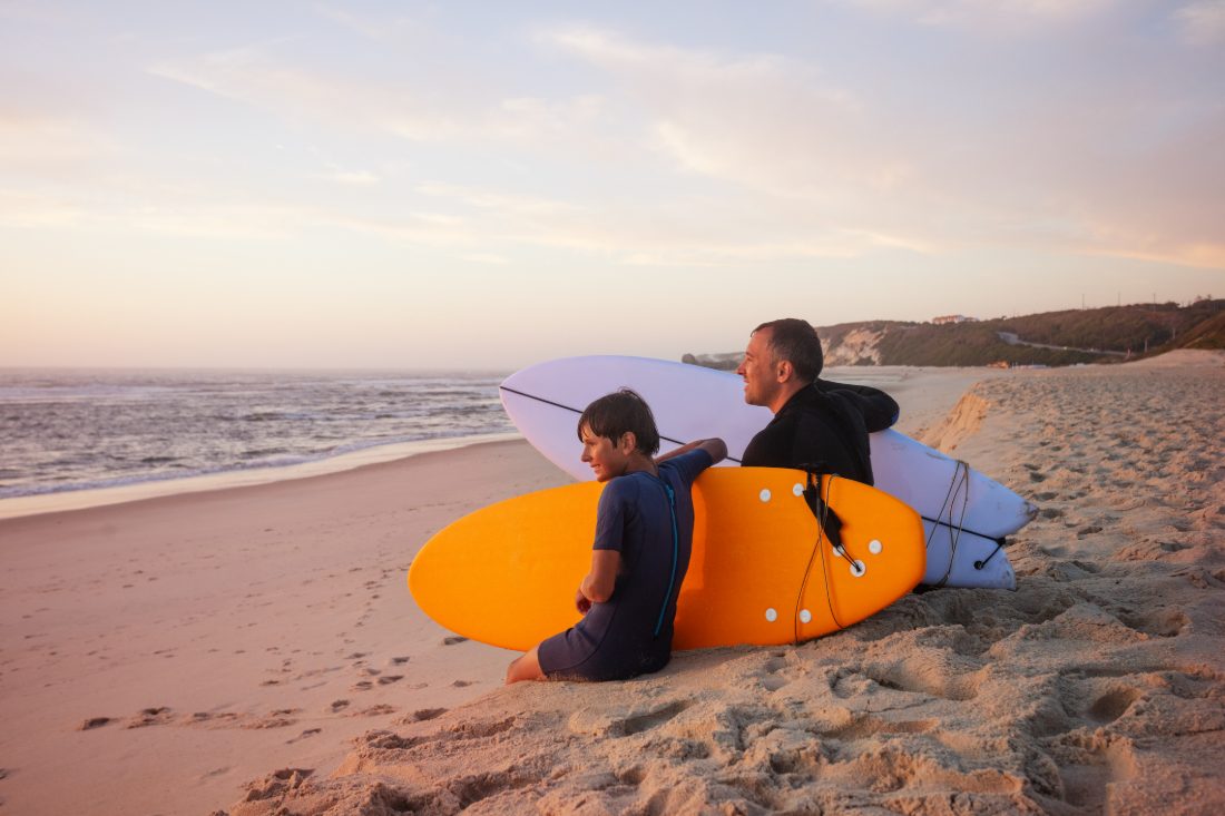 Father and son with surfboards at sunset