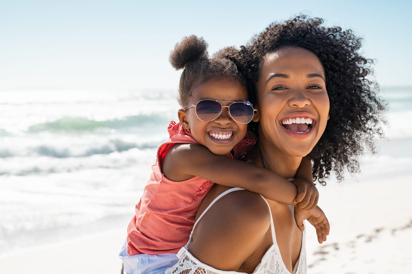 A mother and her young daughter laughing together at the beach